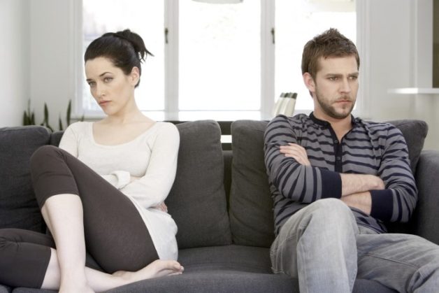 Couple sitting on sofa with arms folded, looking angry